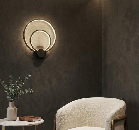 Modern wall sconce on a dark wall with a chair and small table in the foreground.