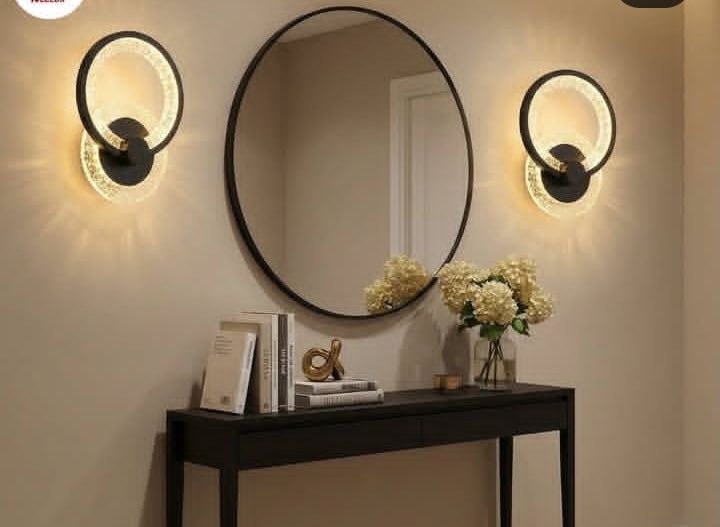 Round mirror with two wall lights on a beige wall above a dark console table.