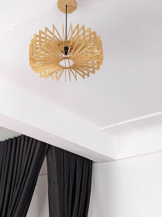 Wooden pendant light fixture on a white ceiling with black curtains below.