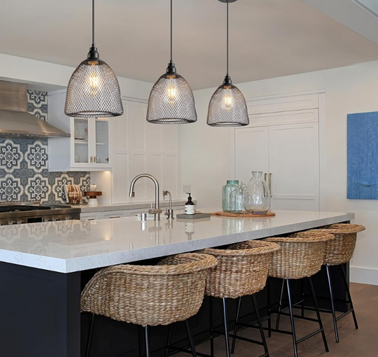 Three black mesh hanging light fixtures illuminating a modern kitchen island with wicker bar stools