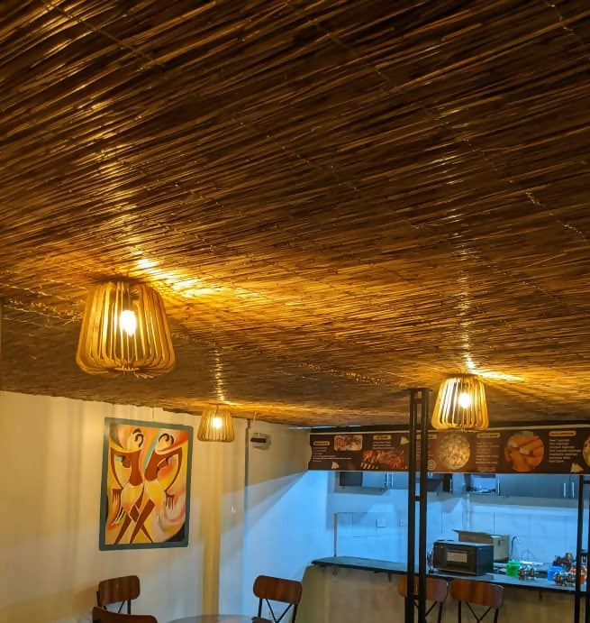 Ceiling with woven design and hanging lights, featuring a painting and menu board in the background.