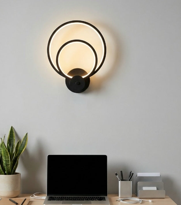 Modern wall sconce with a laptop, plant, and office supplies on a desk against a light gray wall.