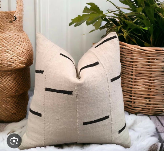 Beige pillow with black line design on a white surface with wicker baskets and greenery.