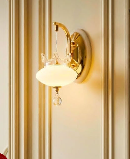 Decorative wall light fixture with gold finish and glass shade on a wall with decorative molding.