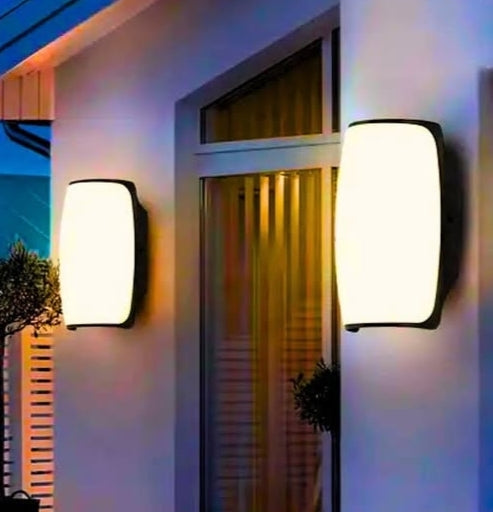 Two outdoor wall lights on a building facade with a window in the background.