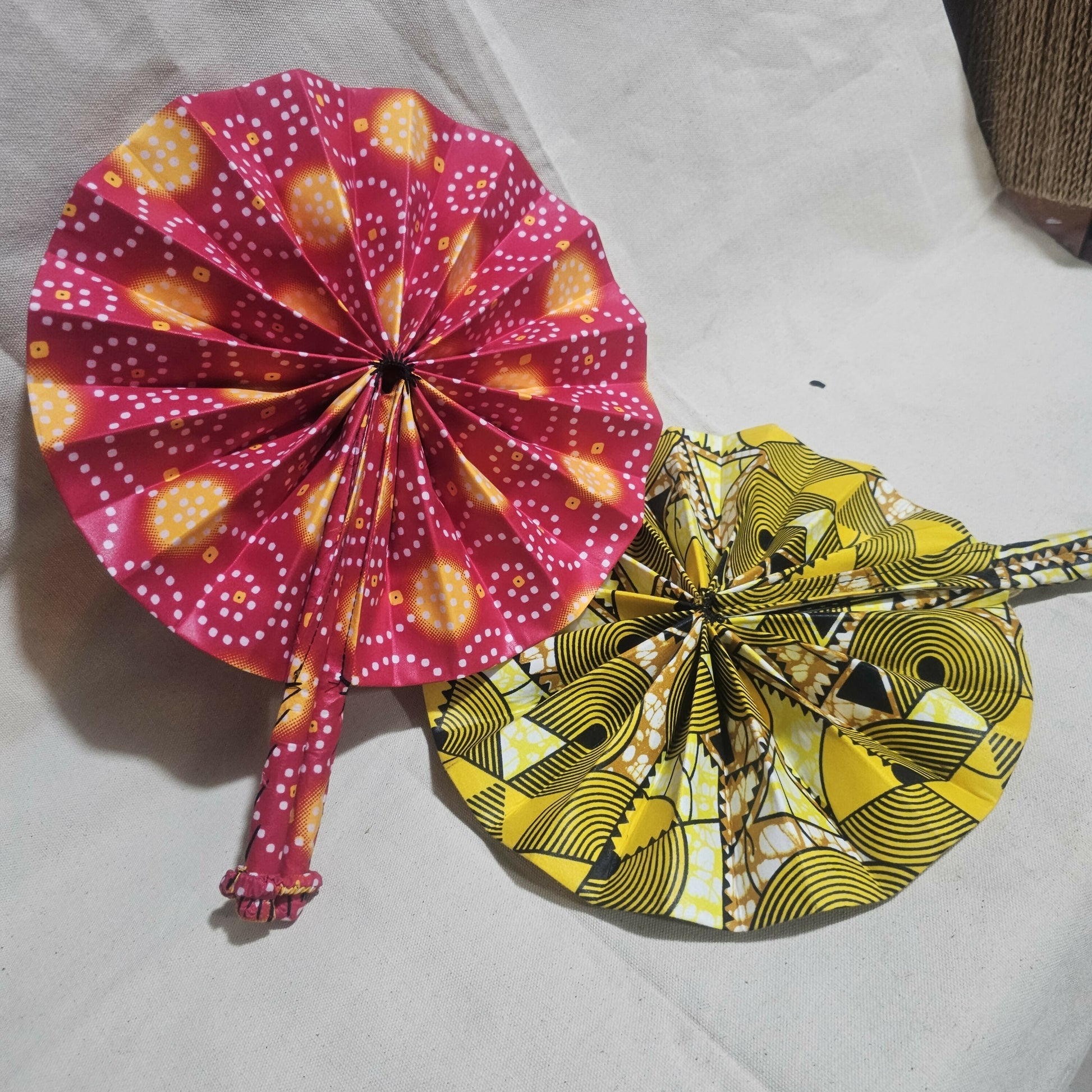 Two decorative fans, one pink with yellow patterns and the other yellow with black patterns, on a white background.