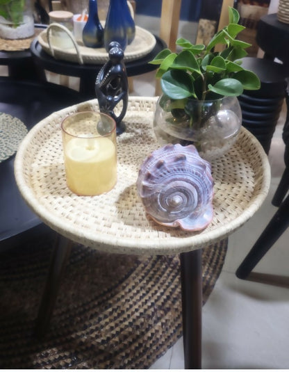 Small wicker table with a candle, seashell, and plant in a room setting.