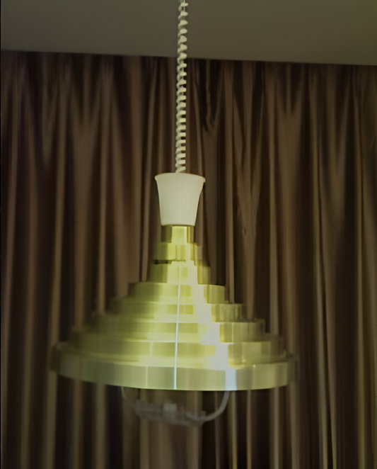 A golden-tiered pendant lamp hanging in front of a brown curtain.
