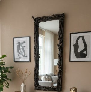 Decorative mirror with natural branch frame on a wall with framed art and a plant.