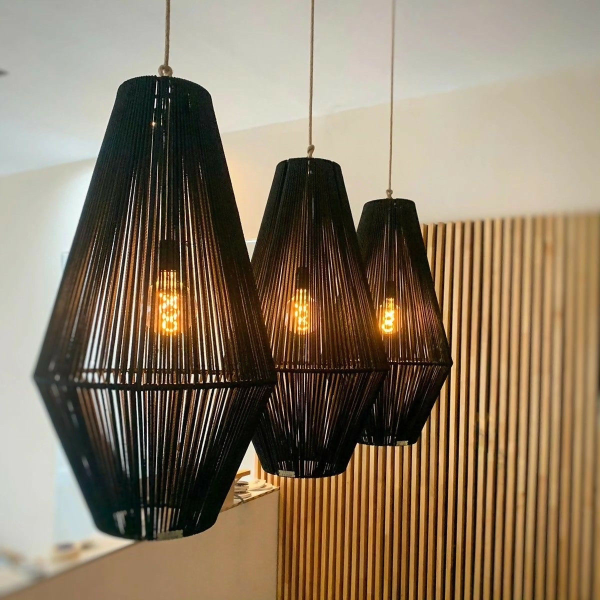 Three black pendant lights hanging in a room with a wooden panel background.