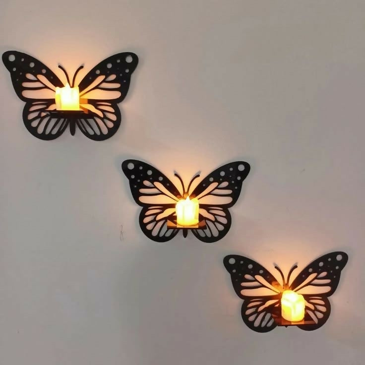 Three butterfly-shaped wall candle holders with lit candles on a plain wall.