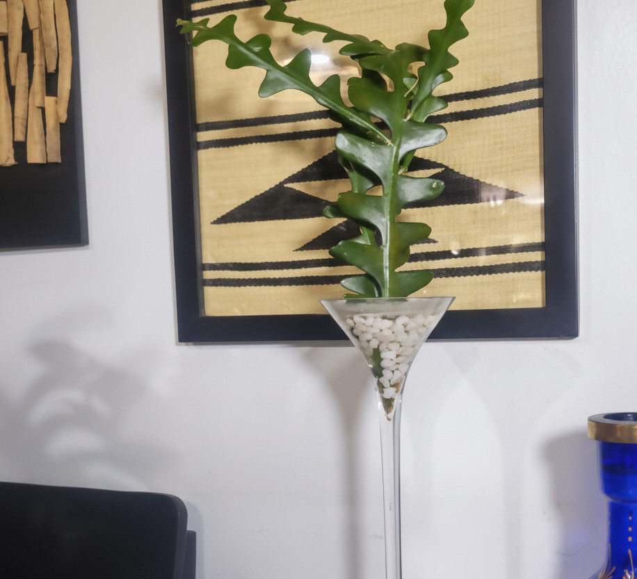 Tall glass vase with decorative plant on a surface with a blue and gold vase in the background.