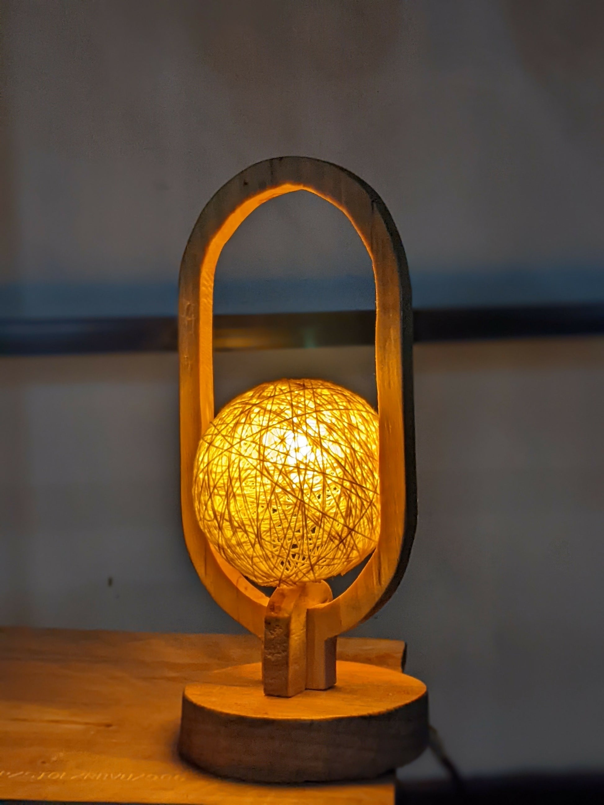 Wooden lamp with a spherical, string-like light bulb on a wooden surface.