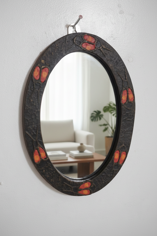 Decorative oval mirror with black frame and red accents on a white wall.