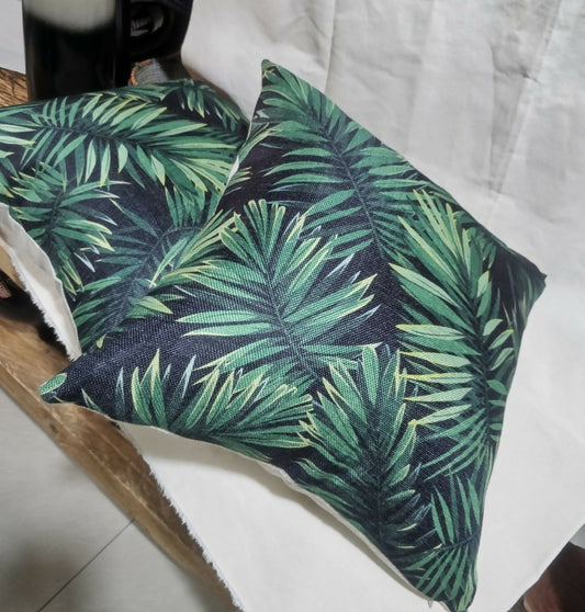 Two green leaf-patterned pillows on a white surface.