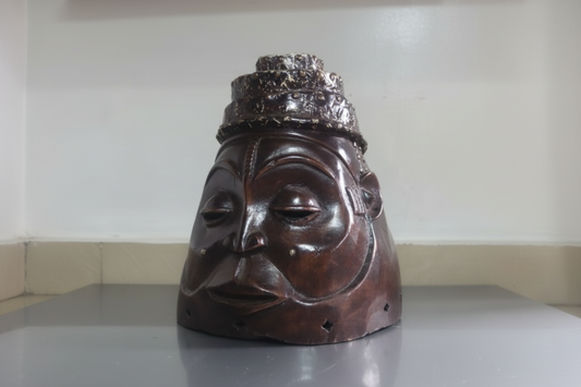 Wooden mask with a crown on a flat surface against a white wall
