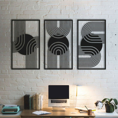 Three black abstract wall art pieces on a white brick wall above a desk with a laptop and books.