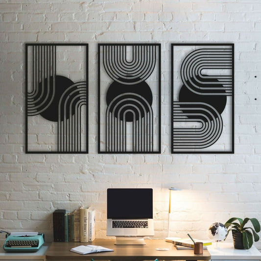 Three black abstract wall art pieces on a white brick wall above a desk with a laptop and books.