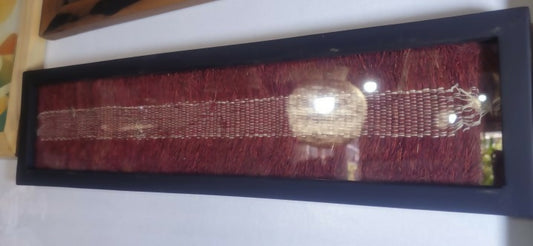 Decorative red ribbon with a gold emblem in a black frame on a white surface.