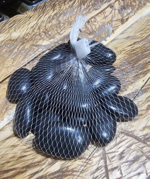 Black stones in a wire mesh bag on a wooden surface